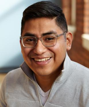 Headshot of a man wearing a V-neck sweatshirt and glasses. 