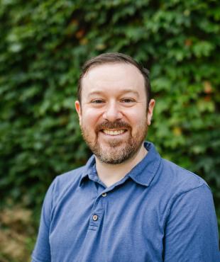 Man in front of greenery smiling for headshot