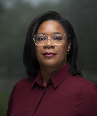 Headshot of woman with black hair wearing a maroon blouse and clear frame glasses.