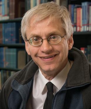 Man smiling with jacket with glasses in front of bookshelves
