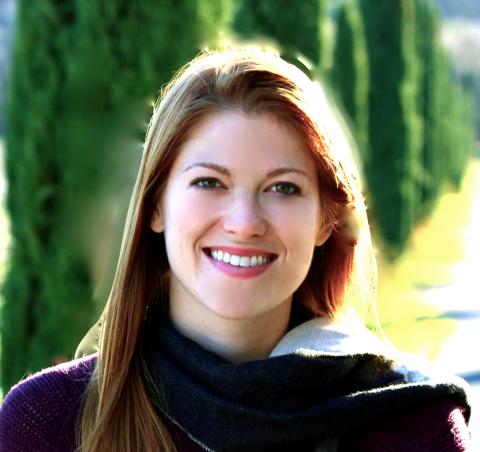 Woman in dark sweater with scarf and red hair standing outdoors smiling