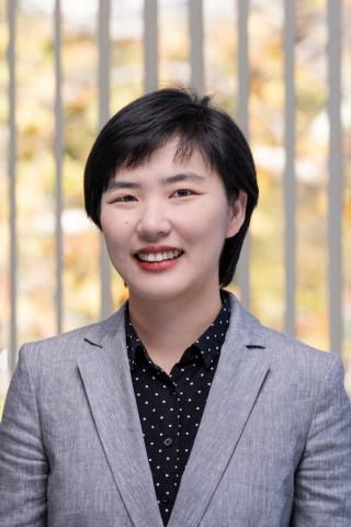 Woman in a grey suit jacket with a black and polka dot shirt smiling