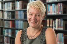 Jessica Darrow, a female-presenting person, smiles towards the camera in a library.