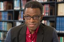 Waldo Johnson, a male-presenting person, smiles towards the camera in a library.