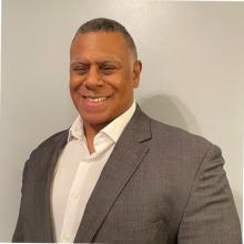 man in grey suit no tie smiling