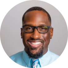 Man in blue shirt and tie with glasses smiling