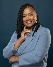 Woman standing with finger pointing under chin smiling in grey suit