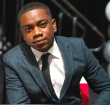 Man in dark blue suit, white shirt with black tie 