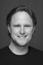 Black and white of man wearing smiling wearing a black tee shirt