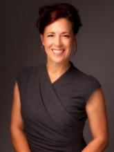 Woman standing and smiling wearing a black blouse with dark brown hair in an updo style