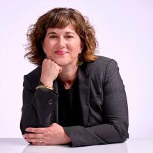 Headshot of Paige Ponder in a grey suit with hand under chin smiling
