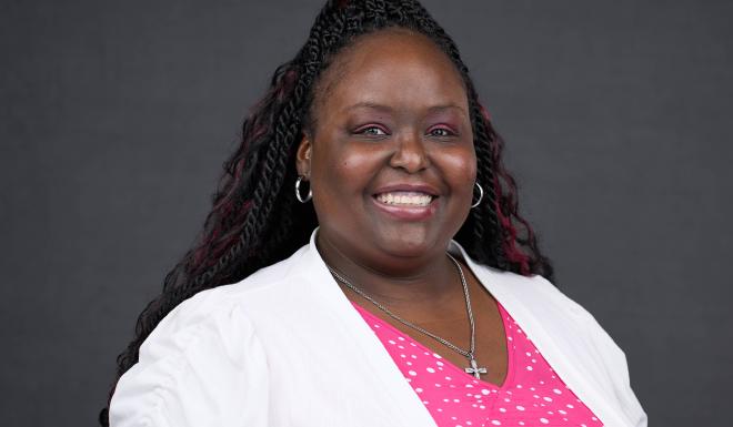 Woman in white shirt with pink and white dots with a ponytail smiling