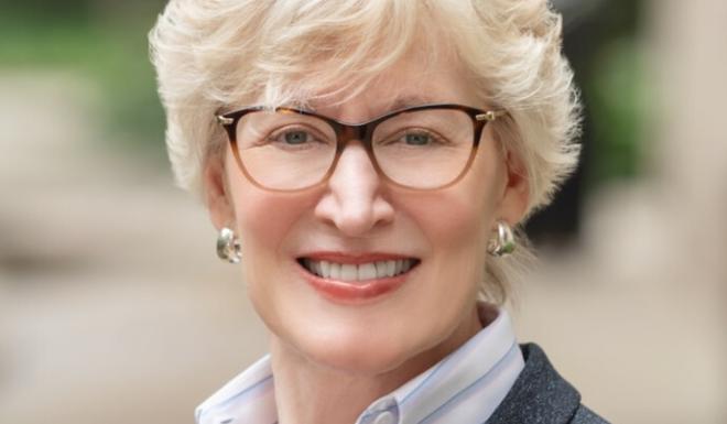 Womn in grey suit with with striped shirt smiling outdoors with glasses