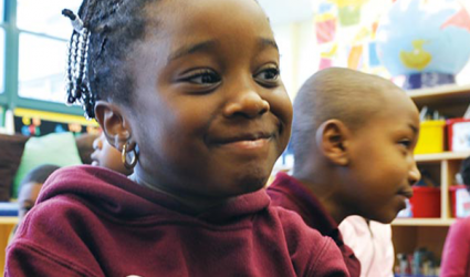 A child in a classroom grins away from the camera.